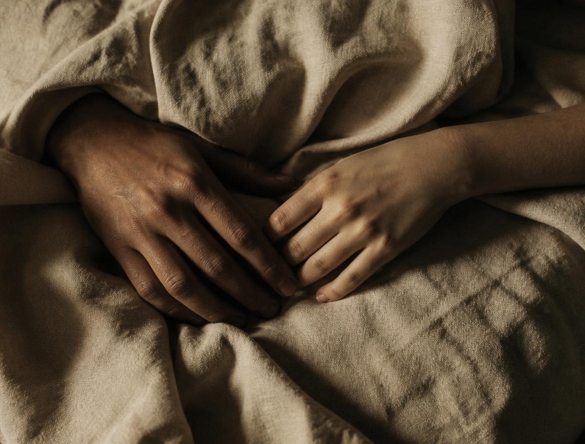 Two hands resting close together on rumpled natural linen in warm light