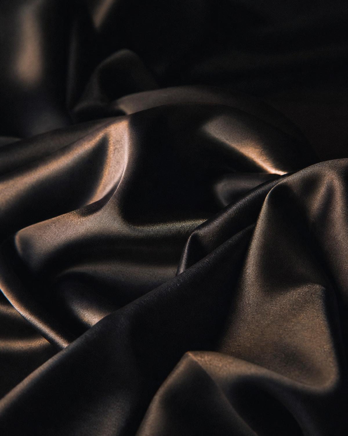 Folds of dark silk catching a single warm light against deep shadow